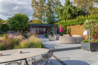 Contemporary entertaining garden featuring porcelain paving, steps, pergola, deck, naturalistic planting, lawn and fire bowl. 