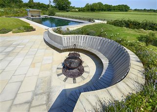 Bespoke wooden bench with fire pit and natural swimming pool beyond