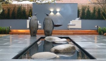 The Penguin Garden.  A contemporary outdoor living space with a central canal of water.  The Penguins are positioned, poised to leap onto the first rock. Lighting creates a strong focal point beyond the Penguins to draw the eye down the garden.