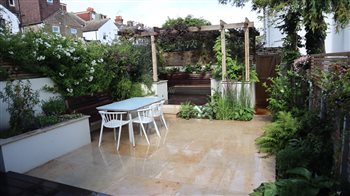 Clean lines softened by climbers and flowers in this courtyard garden in Brighton. A copper spout fountain with glazed green and white tiles emerges from the low wall below the pergola, creates a soothing splash.
