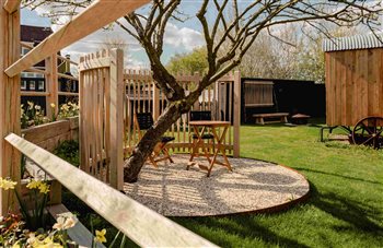 A bespoke curved oak screen creates a cosy seating area under the apple tree without closing out the light or wild flowers to the rear; an oak trellis provides structure for an evergreen climber, both in the Spirilis design. 